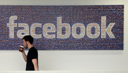 A Facebook employee walks past a sign at Facebook headquarters in Menlo Park.