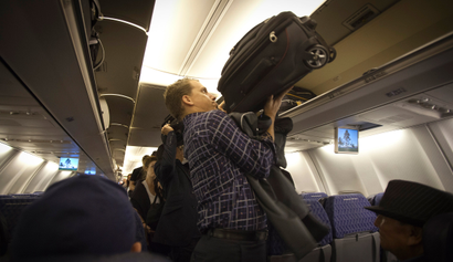 A passenger places his luggage into the overhead bin before an American Airlines flight from Miami to New York December 10, 2013.