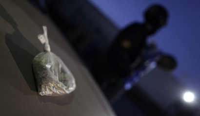 A bag of cannabis sits on the hood of a car as a suspect is arrested.