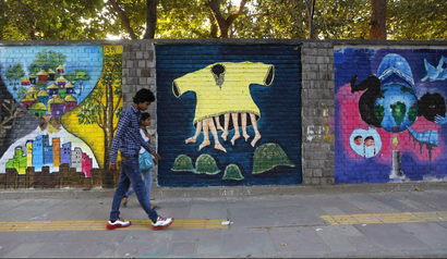 Commuters walk past graffiti themed "Design the Change" on a wall of the University of Delhi campus