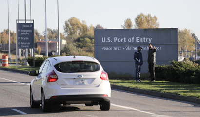 In this photo taken Oct. 9, 2019, two pedestrians take a photo at an entry sign as traffic enters the United States from Canada at the Peace Arch Border Crossing, in Blaine, Wash.