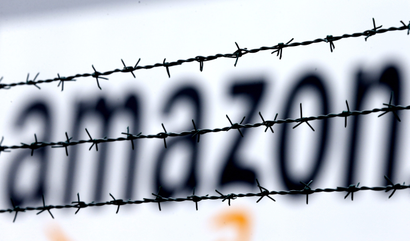FILE - In this Feb. 19, 2013 file photo, the internet trader Amazon logo is seen behind barbed wire at the company's logistic center in Rheinberg,Germany. The European Union is telling member state Luxembourg to get $295 million in back taxes from Amazon in Brussels’ latest regulatory move targeting U.S. tech companies accused of tax avoidance, it was reported on Wednesday, Oct. 4, 2017. (AP Photo/Frank Augstein, File)