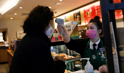 Worker uses a thermometer to check the temperature of a customer as she enters a Starbucks shop as the country is hit by an outbreak of the new coronavirus, in Beijing