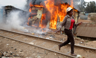 A woman walks past a burned shack, in Kibera slum, in Nairobi, Kenya.