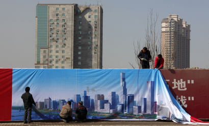 Workmen install a poster onto a wall surrounding a construction site showing an artist's impression of the new business district of Binhai, located in the Yujiapu financial zone on the outskirts of the city of Tianjin March 2, 2011. Round-the-clock construction is transforming muddy ground into what officials boast will be the world?s largest financial zone, a monument to the ambitions that have driven China to dizzyingly fast growth. When the country?s leaders gather for their annual parliament in Beijing on Saturday, they will endorse plans to tap the brakes on the speeding economy, a shift that is needed to keep inflation and debt, under control for now, from becoming far more troublesome. But they need only make the one-hour trip to the financial district sprouting up in Tianjin to see how hard-driving local officials, cash-rich state-owned banks and the soaring aspirations of people seeking a better life are imperiling their designs for slower, steadier growth. REUTERS/David Gray