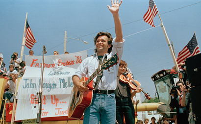 Singer John Cougar Mellencamp waves to the crowd in Chillicothe, Mo., as he arrives on stage to perform at the farmer's rally, May 7, 1986. The three-song concert was held in the parking lot of the Livingston County, Mo., FmHA office. Local farmers have occupied that site since March 17 to protest the policies of the county FmHA supervisor. (AP Photo)