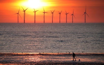 A man stands on the beach as the sun sets behind the Burbo Bank wind farm near New Brighton, Britain, May 22, 2018.