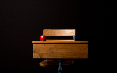 A red apple sits on a wooden desk in front of a black backdrop.