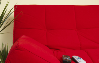 An image of a red futon sofa with two remotes.