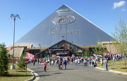 The silver Memphis Pyramid stretching up into the sky with the Bass Pro Shops logo on it, as people stream in on a sunny day.