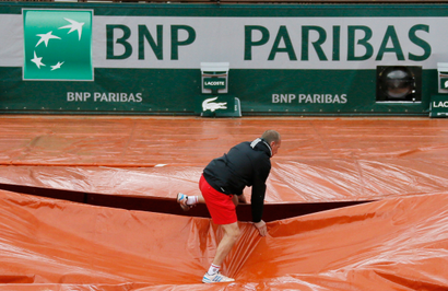 A grounds crew member covers the clay court from rain near the logo of BNP Paribas during the French Open tennis tournament