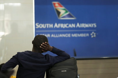 A passenger is seen at the South African Airways (SAA) customer desk with his head resting on his hand and bag in a position that shows frustration. The picture is taken from behind him.