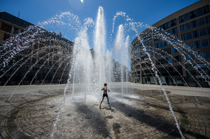 A kid runs through a giant water fountain in the middle of a city street. 