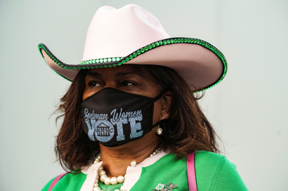 A woman with a cowboy hat wears a mask reading "vote"