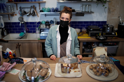 A woman wearing a mask behind baked goods at a coffeeshop or bakery
