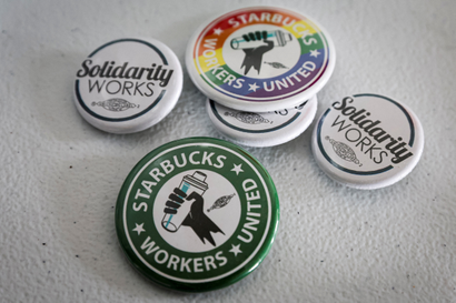 Five buttons showing support for a Starbucks Union are laid on a white table.