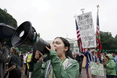A woman in a green rain jacket yells into a bullhorn outside the White House