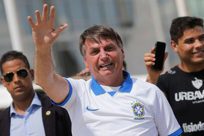 Brazilian president Jair Bolsonaro, who has been criticized for not taking the coronavirus seriously, waves at a crowd while wearing a soccer shirt.