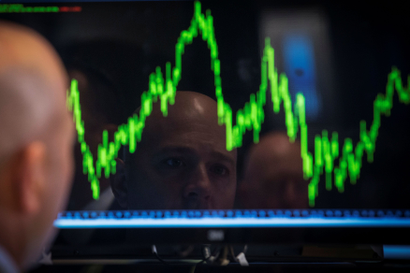 A bald man looks at a screen showing a volatile stock chart on the floor of the New York Stock exchange.