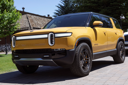 A yellow Rivian electric SUV is parked along a grass patch.