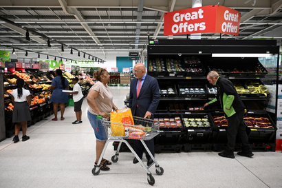 A woman with a cart of groceries stops to talk to a man in a suit.