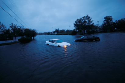 An abandoned car sits flooded on a submerged road at dusk.
