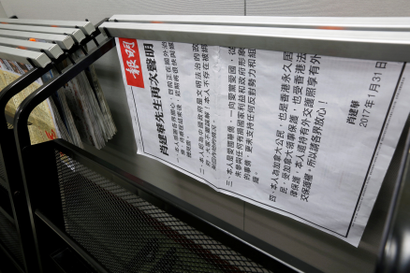 A printed rectangular sign is stuck sideways underneath the bannister of a glass-walled staircase. The paper is printed in black and white and has a statement written in traditional Chinese characters.