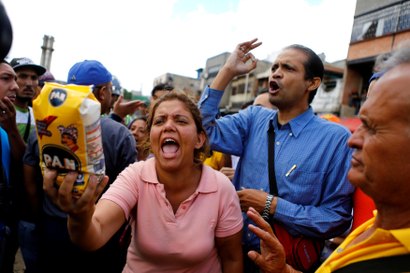 A woman shows a flour package outside a supermarket as they shout slogans over food shortage in Caracas, Venezuela