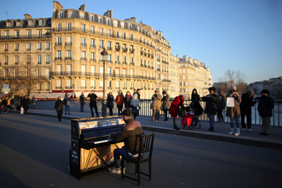 People stop to listen to a man who plays a piano on a bridge over the Seine River in central Paris