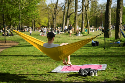 A man in a baseball hat sits in a yellow hammock in a park.