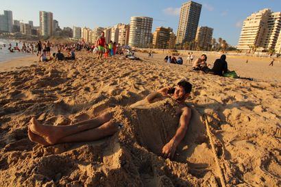 A man talks on his mobile phone while covered in sand on the beach in Beirut.