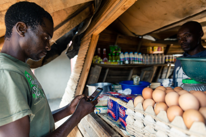 Aaron Munyoro, who is unemployed and lives with his elderly mother, makes a payment from his mobile phone for basic food items including bread at a local tuck shop in Epworth, on the outskirts of Harare, on December 10, 2019.