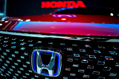 A close up picture of a car grill with the Hondo logo is shown, with the word Honda glowing in the background.