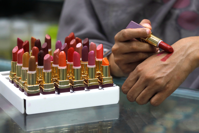A shop attendant applies lipstick on her hand for a customer to check the shade at a store in Peshawar