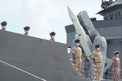Soldiers stand on a boat with a missile in the background.