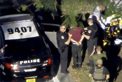 A man placed in handcuffs is led by police near Marjory Stoneman Douglas High School.