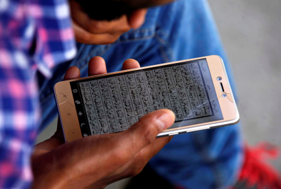 A man reads the Koran on his mobile phone outside a mosque during the holy fasting month of Ramadan, in Srinagar