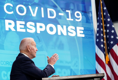 Side profile US president Joe Biden, who is speaking in front of a blue sign that reads "COVID-19 RESPONSE."