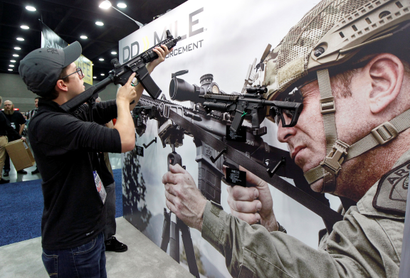 A man holds up a gun next to a large billboard of a Daniel Defense ad at a prior NRA convention.