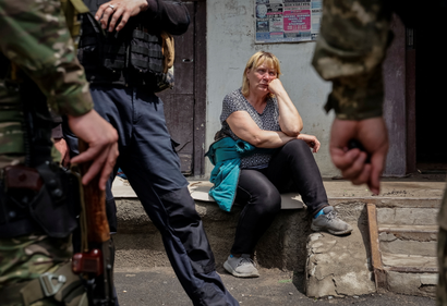 A local resident sits near her apartment building, as police officers stand, as Russia's attack on Ukraine continues, in Lysychansk, Luhansk region Ukraine.
