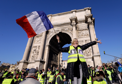 A demonstrator wearing her yellow vest waves a national flag during a protest in front of the Arc de Triomphe of the Porte d'Aix, in Marseille, southern France, Saturday, Dec. 29, 2018. The yellow vest movement held several peaceful demonstrations in cities and towns around France, including about 1,500 people who marched through Marseille.