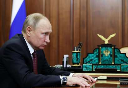 Putin stares from a seat in a gilded office.