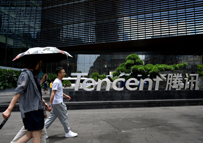 People walk in front of a sign that reads Tencent.