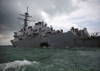 The U.S. Navy guided-missile destroyer USS John S. McCain is seen after a collision, listing and with a huge hole at the waterline.