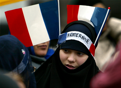 A young muslim girl with two French flags and a headband which reads "Fraternity" pulled over her headscarf.