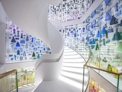 A spiral staircase is surrounded by Dior luxury purses and shoes on the wall in the brand's Paris flagship.