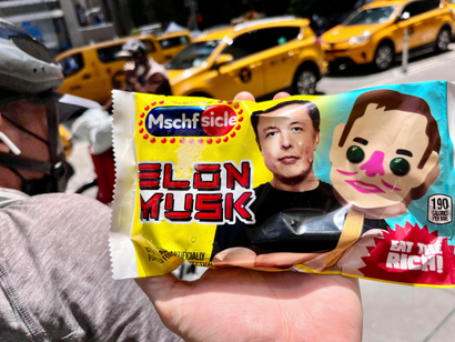 A hand holds up the packaging for the Mschf Elon Musk popsicle.