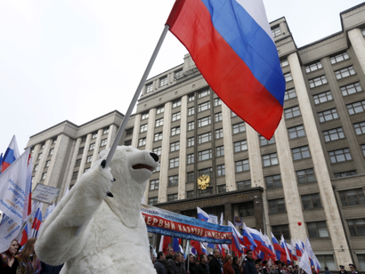 A person in a polar bear costume marches carrying a Russian flag in front of the State Duma