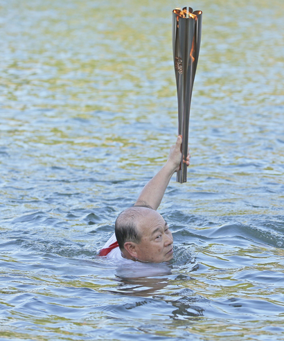 A Tokyo Olympic torch relay participant swims in a river while carrying the Olympic flame in Usuki
