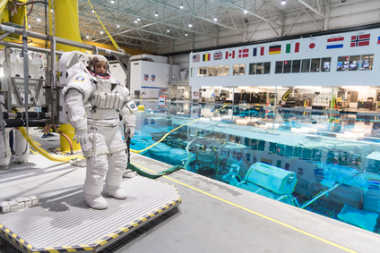 Jessica Watkins, clad in an astronaut suit, stands next to a pool where she will train for spacewalking.